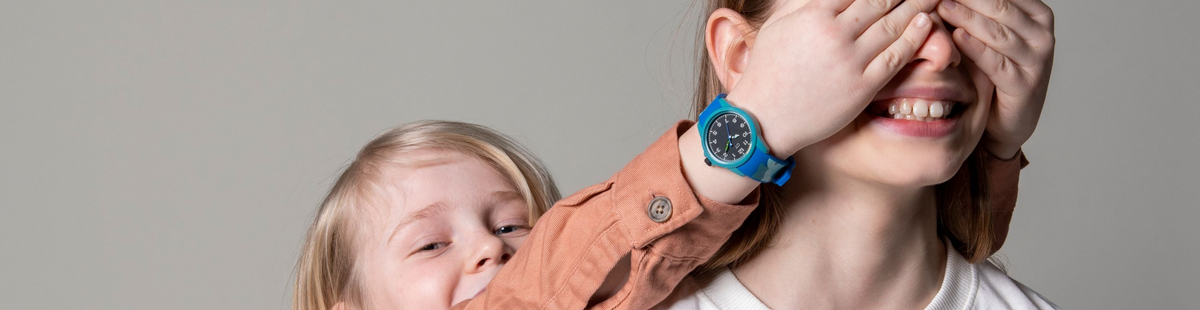 Zwei Kinder spielen miteinander, während eines eine blau-türkise Cool Time Kids Kinderuhr mit analogem Zifferblatt am Handgelenk trägt – fröhliche Alltagsszene mit Kinderarmbanduhr.